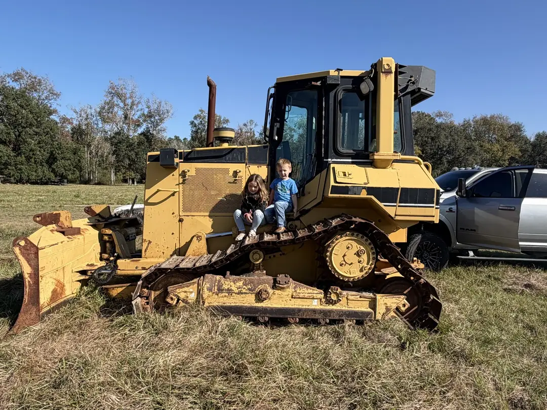 Two young children sitting on the track of a Caterpillar dozer in an open field